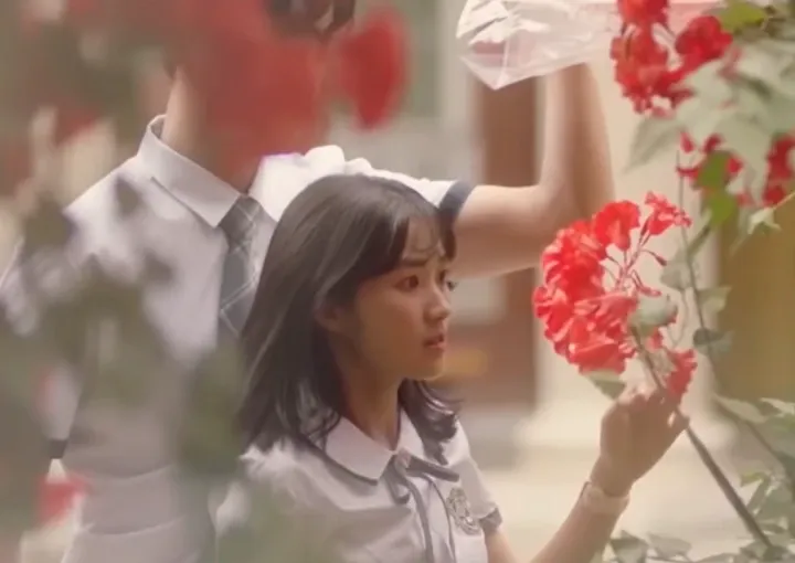 Момиче с училищна униформа посяка към червен цвят на дърво. 