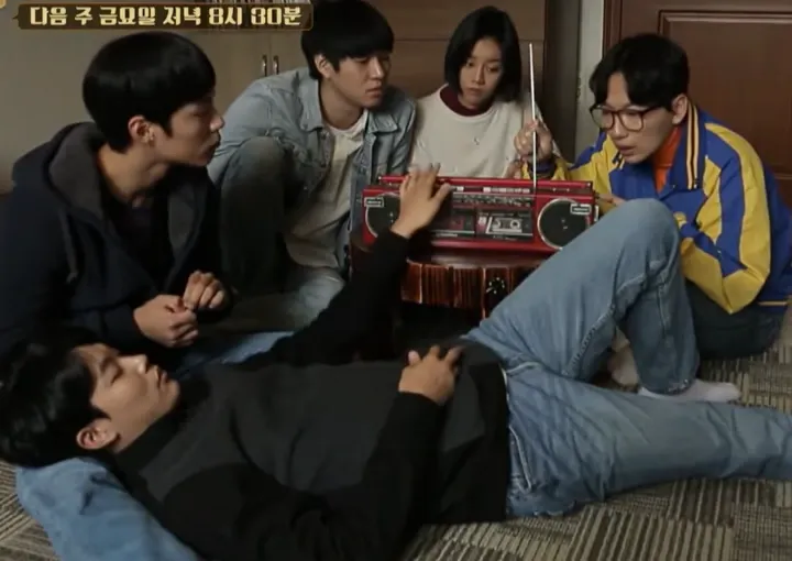 4 момчета и 1 момиче са се събрали около стар касетофон. Едно от момчетата лежи. 